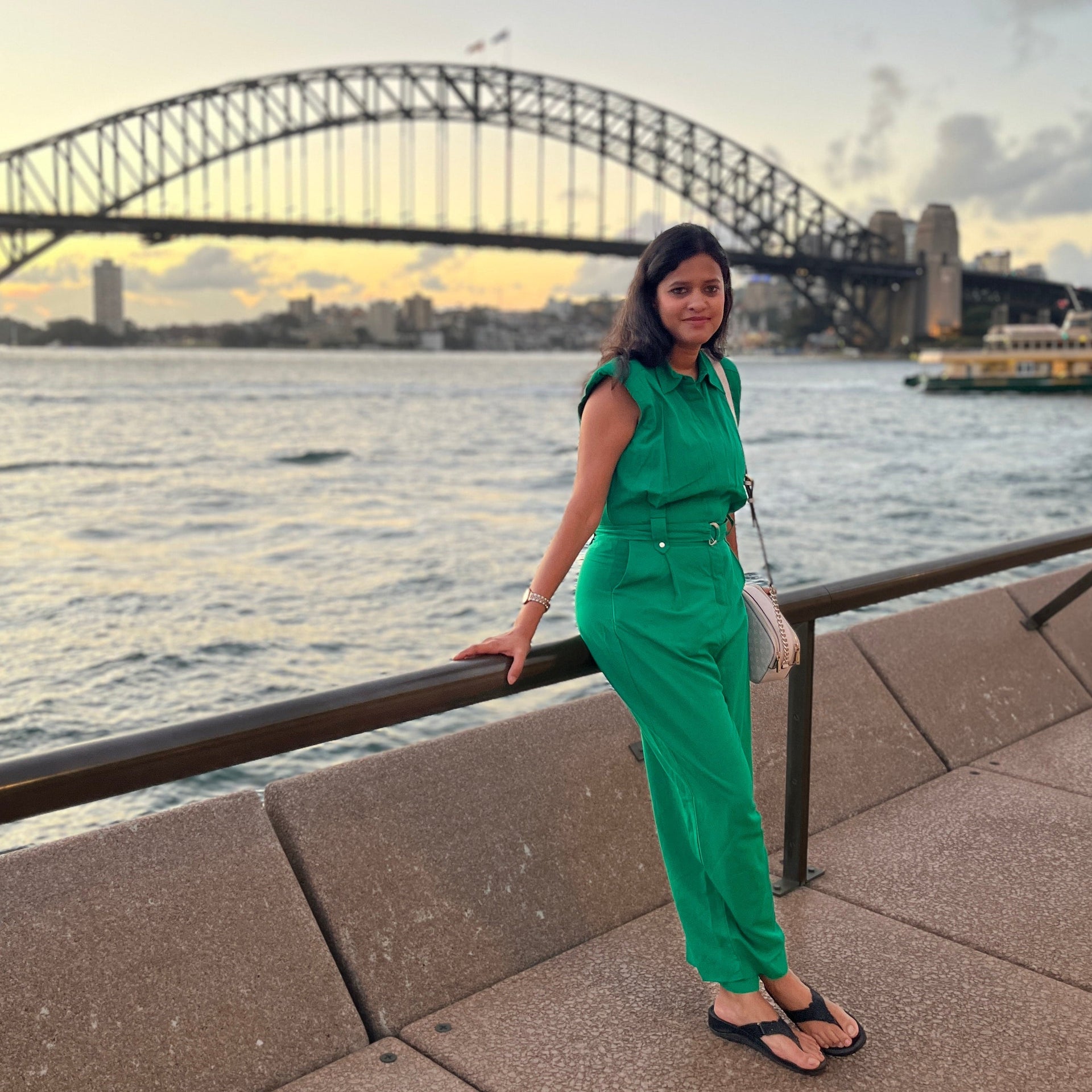 Indian Woman in a modern green outfit standing by a waterfront with a bridge in the background