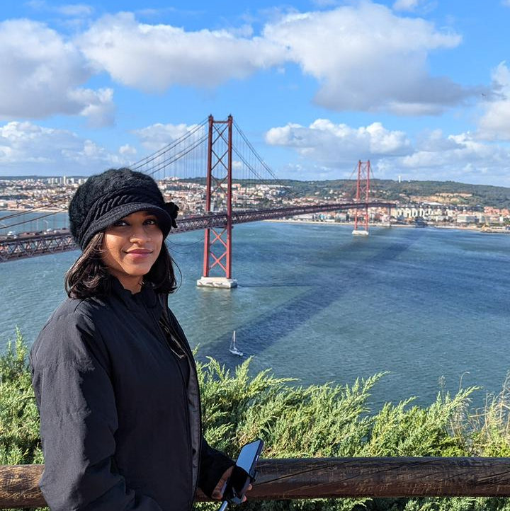 Indian Girl in contemporary clothing standing in front of a scenic view with a bridge and water body